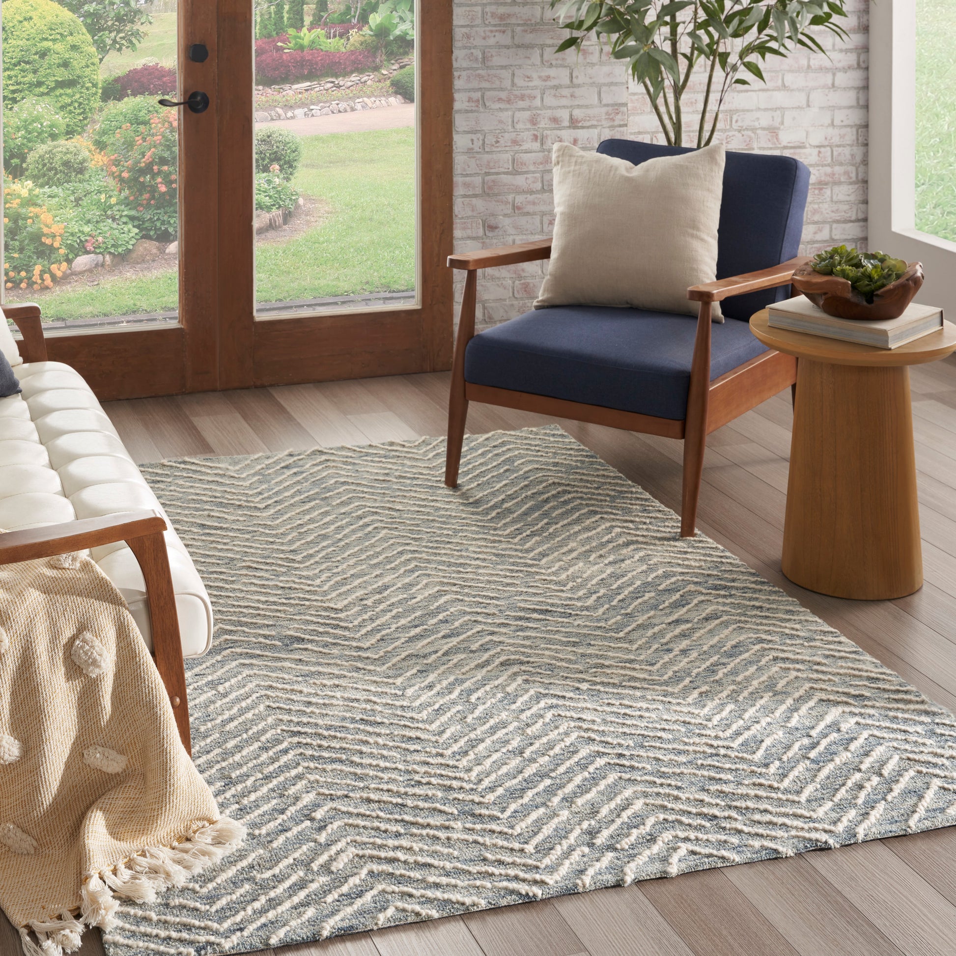 Mid-century living room with navy blue fabric chair, round wood side table, beige pillow, and blue-taupe zigzag rug.