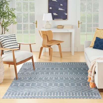 Blue geometric area rug on light wood floor in bright living room with white furniture and natural wood chairs.