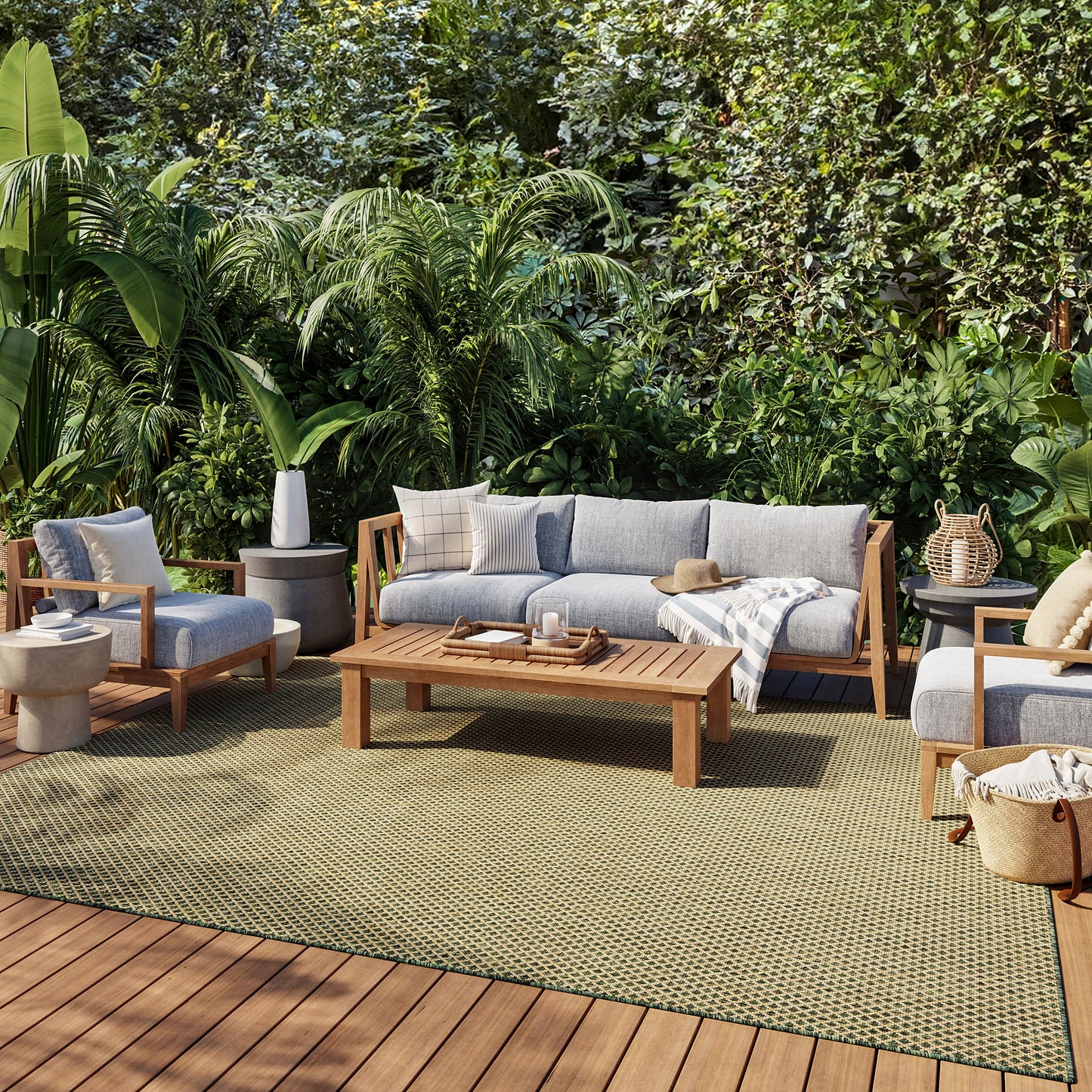 Outdoor lounge set with gray-cushioned wood-framed sofa, chairs & coffee table on a green rug amid lush tropical plants.
