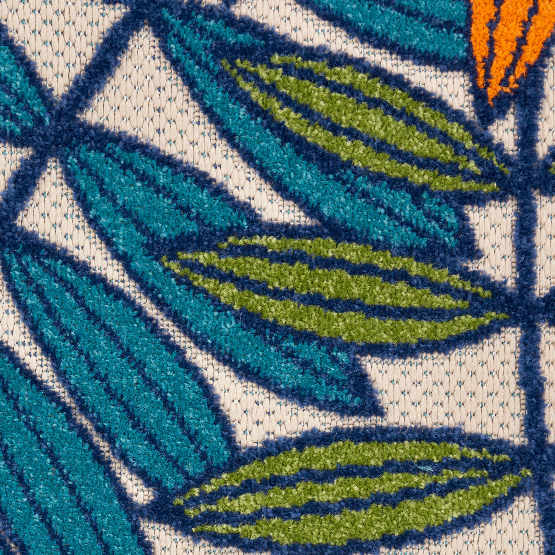 Close-up of teal and olive tropical leaf embroidery on beige woven rug; bold textured pattern.