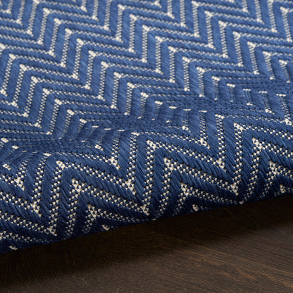 Close-up of blue woven fabric with white chevron zigzag pattern; thick upholstery rug/throw textile on dark wood.
