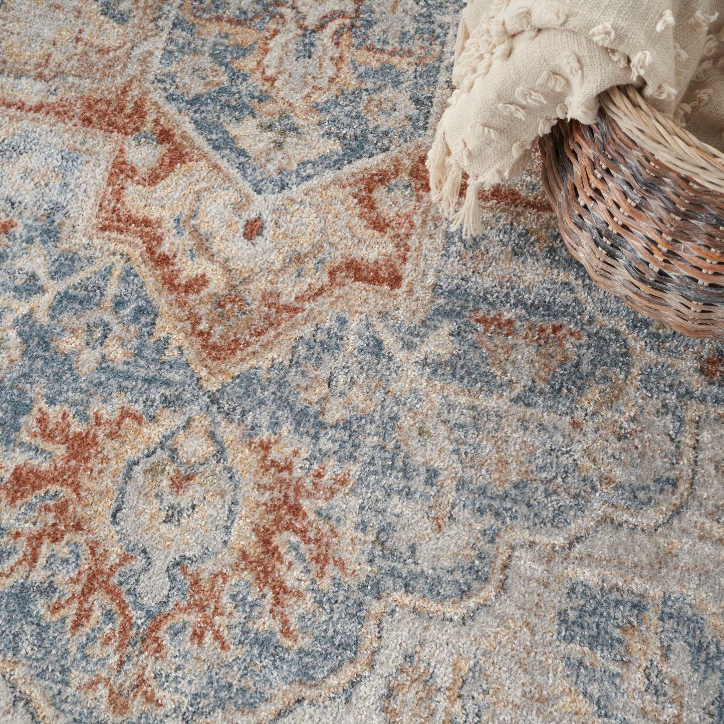 Muted blue, beige and rust oriental wool rug with medallion pattern; cream tasselled throw in a wicker basket.