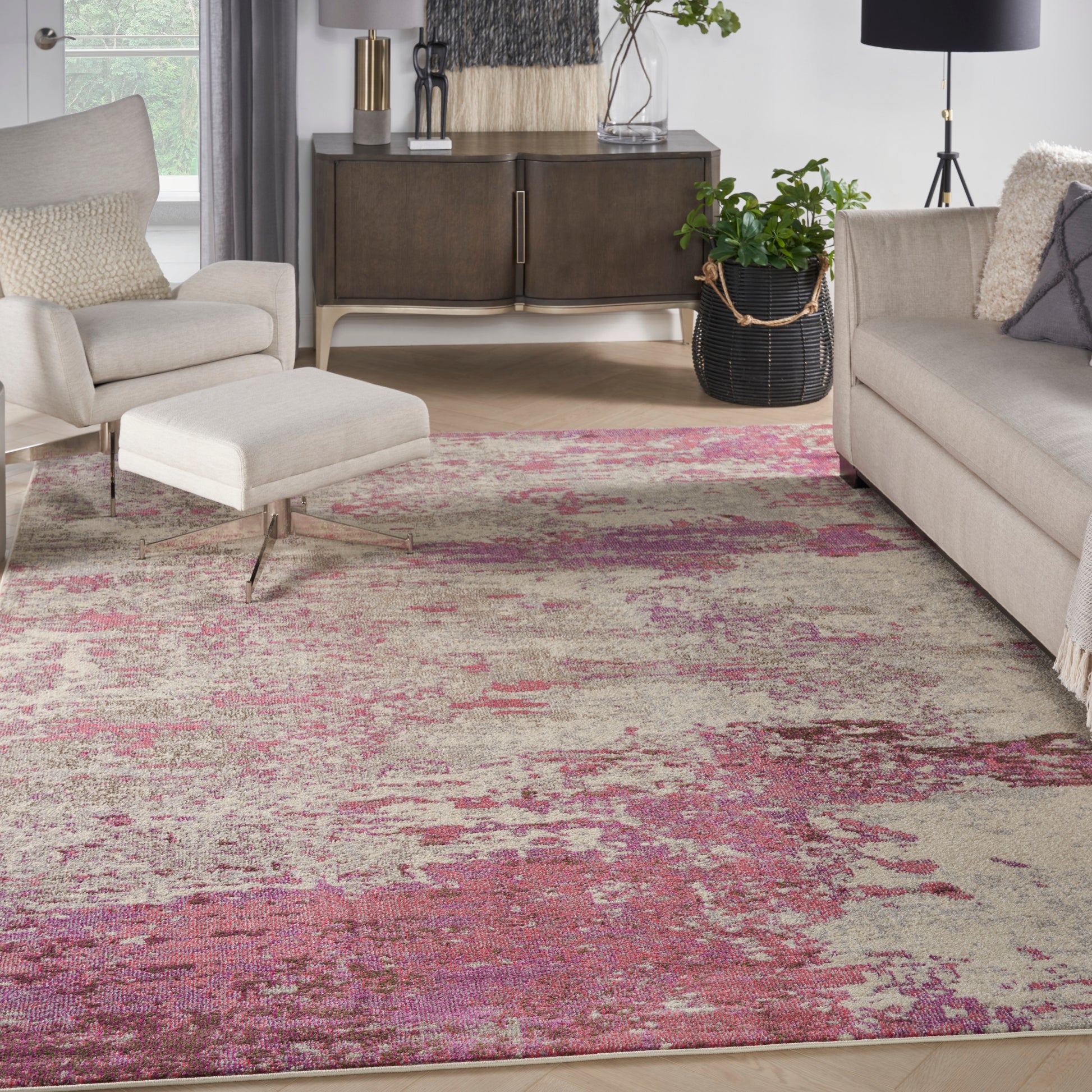 Modern living room with pink-beige abstract rug, beige sofa and ottoman, dark wood console, plant, and black floor lamp.