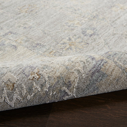 Light gray-blue patterned rug with a soft pile and rolled edge on dark wood floor.