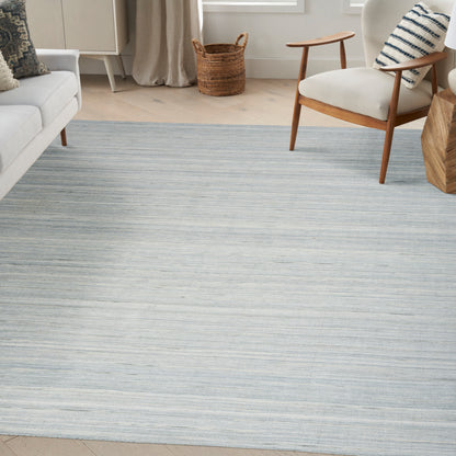 Blue-gray striped rug on pale wood floor with a white sofa, mid-century armchair, and woven basket in a bright living room.