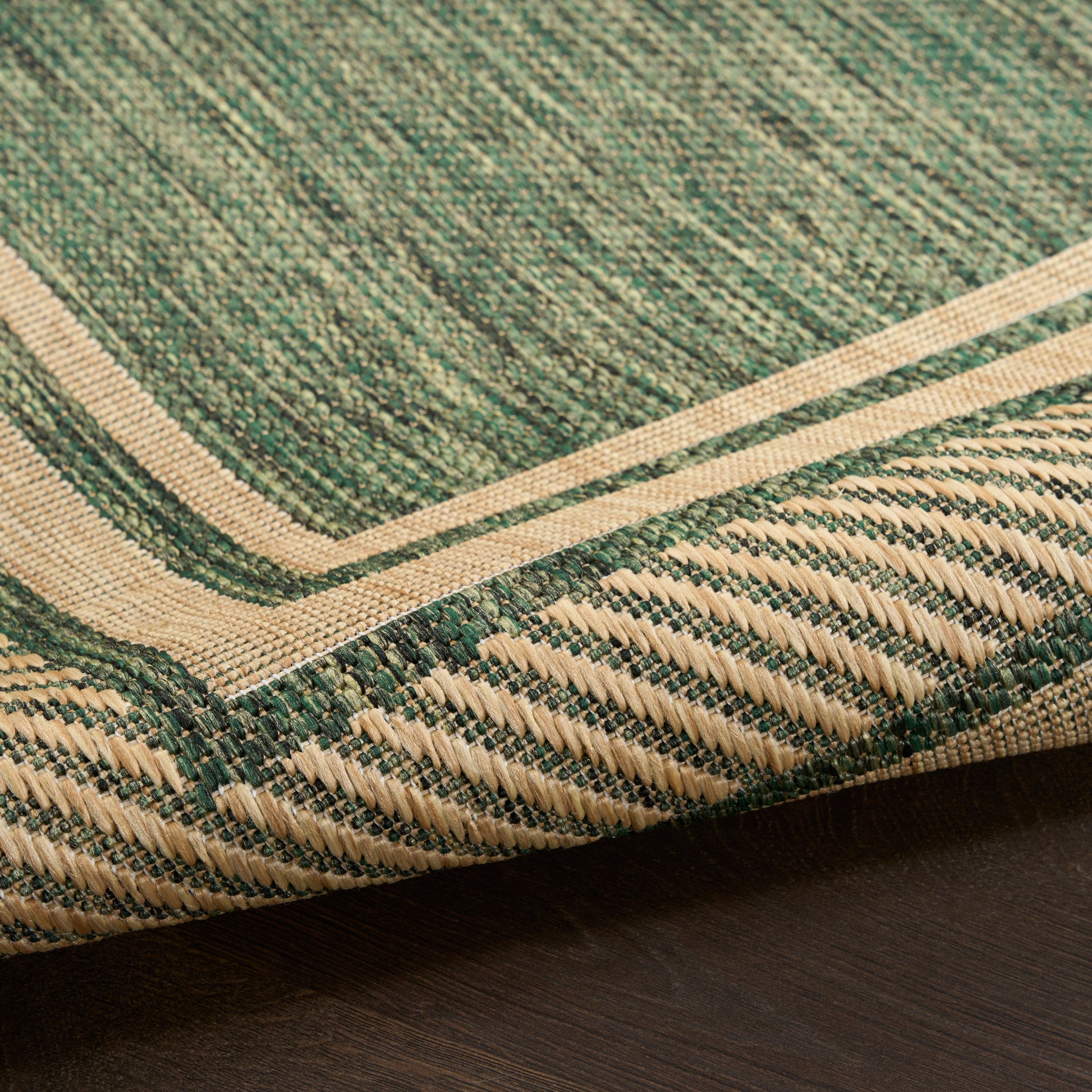 Green woven rug with natural beige border and textured stripe on dark wood floor.