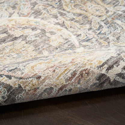 Muted floral-pattern rug in beige, gray, cream and blue tones with a folded edge resting on dark wood floor.