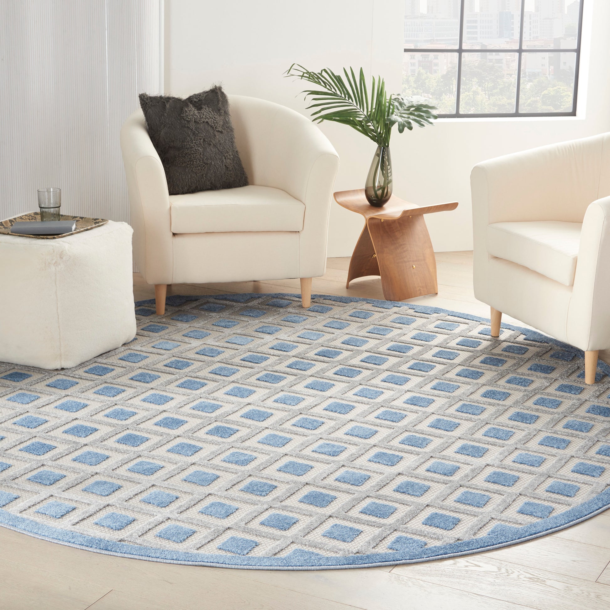 Cream armchairs around a circular blue and beige geometric rug; wooden side table with a plant in a glass vase, bright living room.