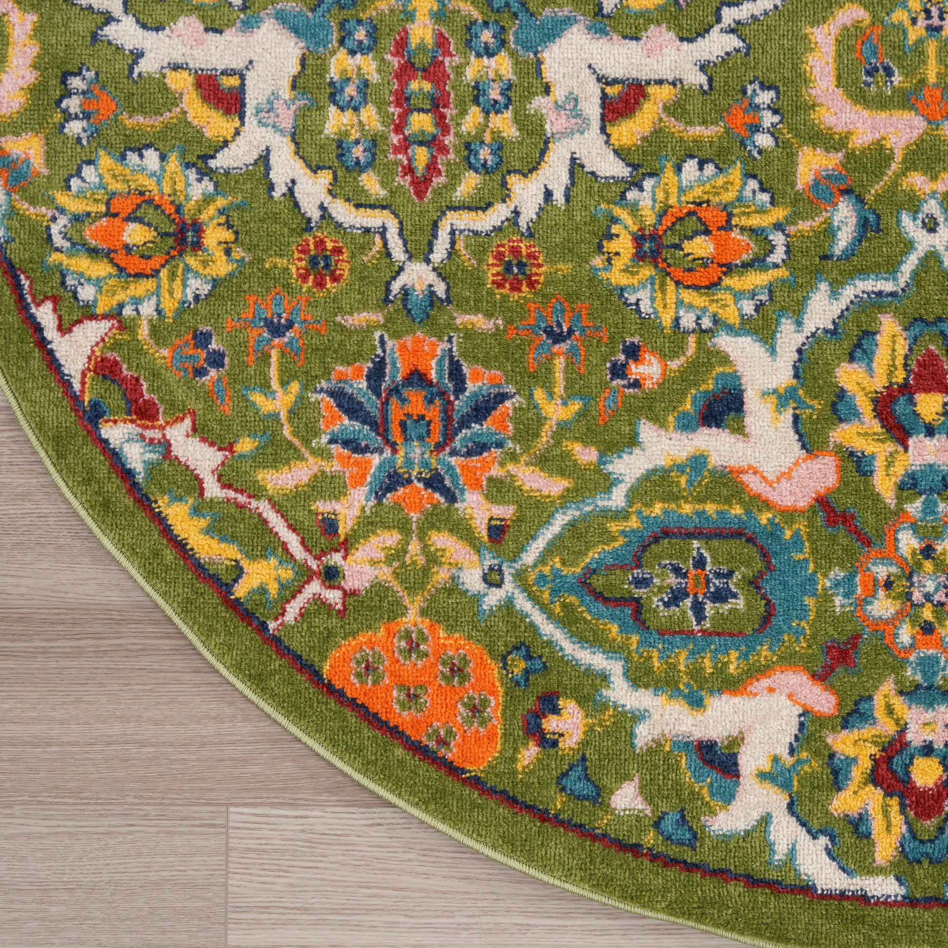 Round green oriental rug with vibrant multicolor floral pattern and bold border on a wooden floor.