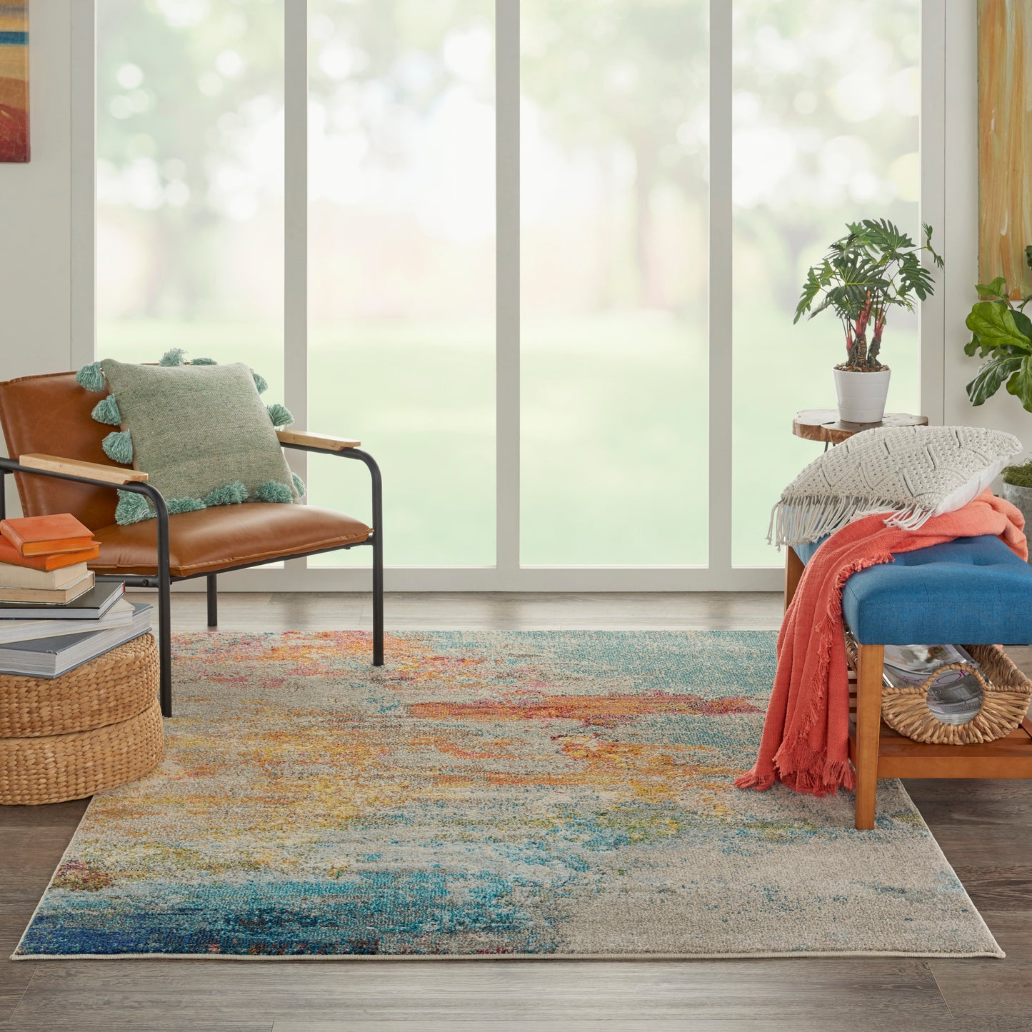 Bright living room with a colorful area rug, brown leather chair, blue cushioned bench, potted plant, and cozy throws.