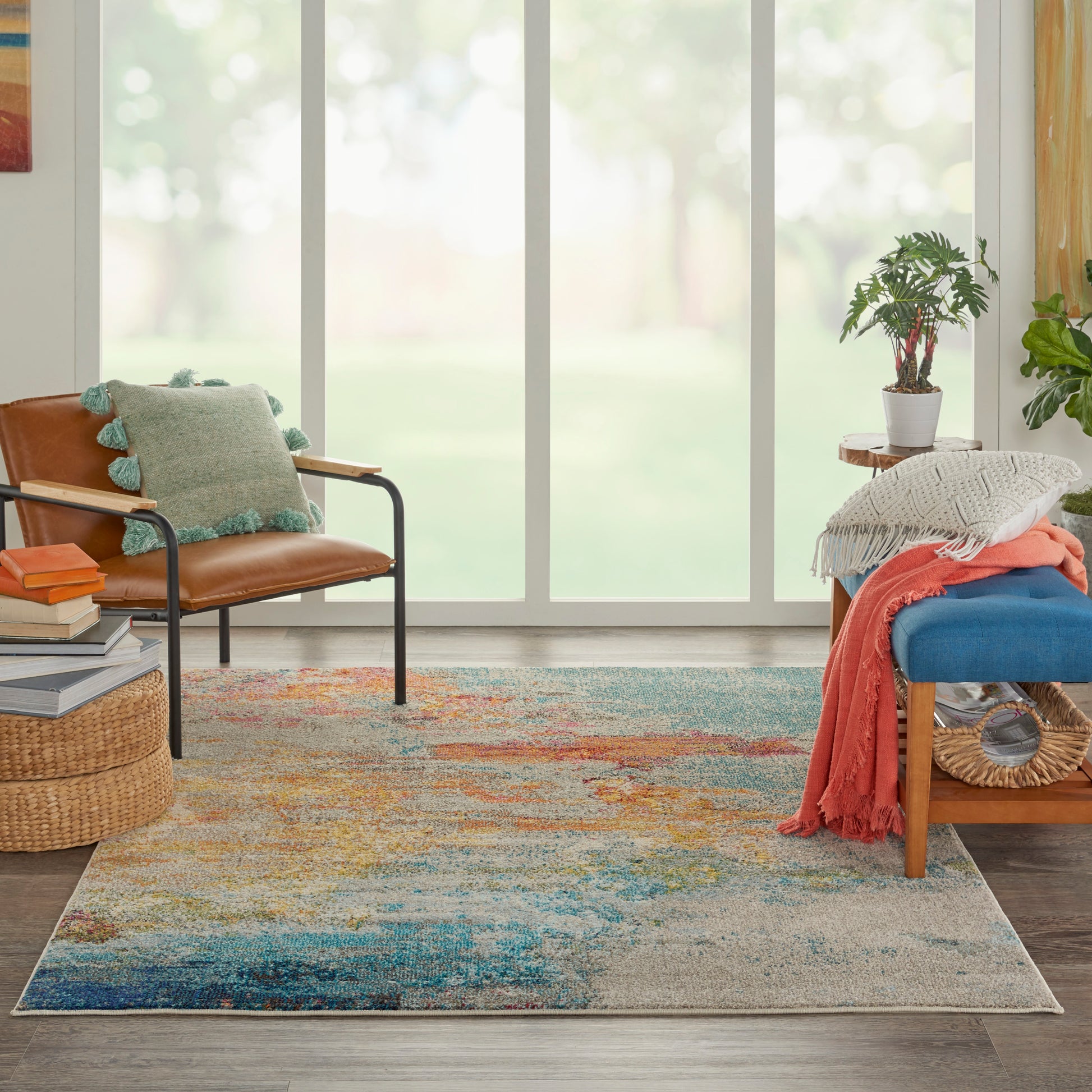 Bright living room with a colorful area rug, brown leather chair, blue cushioned bench, potted plant, and cozy throws.