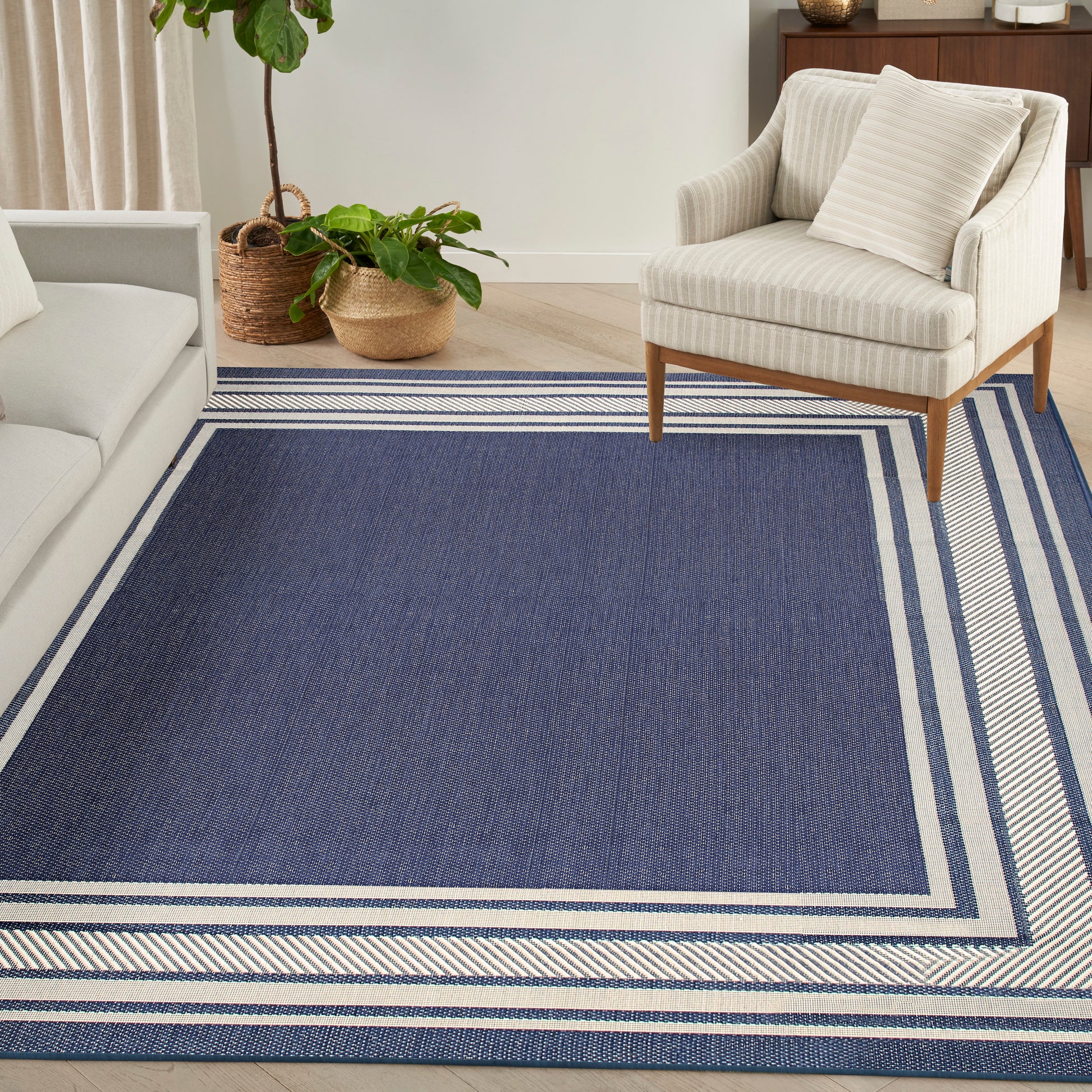 Navy blue area rug with double light borders in a living room, paired with beige striped armchair & sofa.