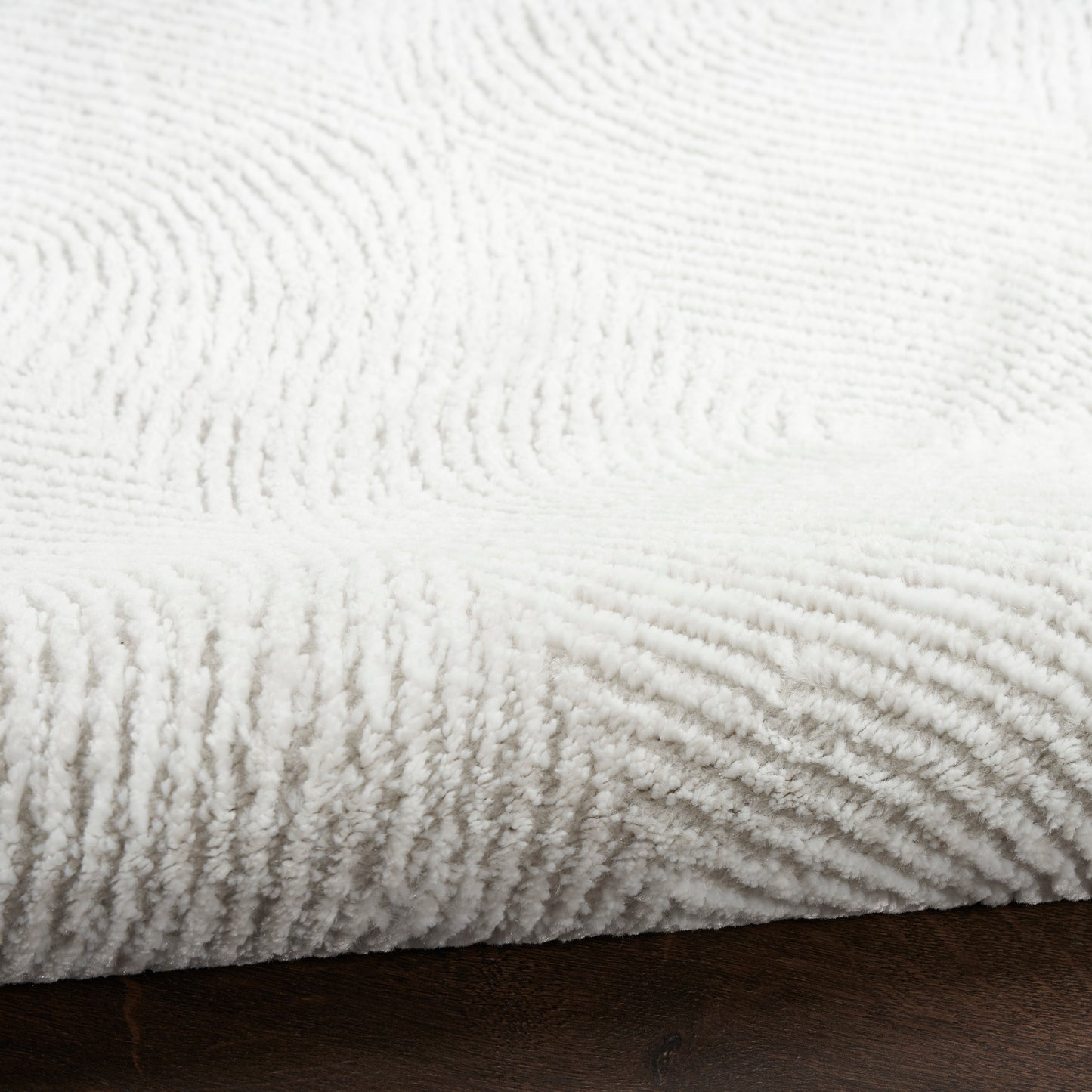 White plush throw blanket with ribbed texture, cozy and soft on a dark wooden surface.