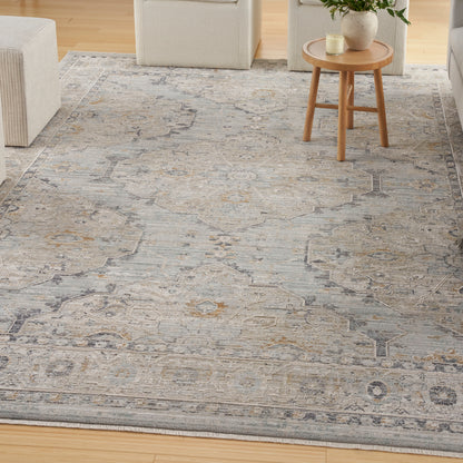 Blue-gray woven oriental area rug with gold accents in a living room, beige seating, and round wooden side table.