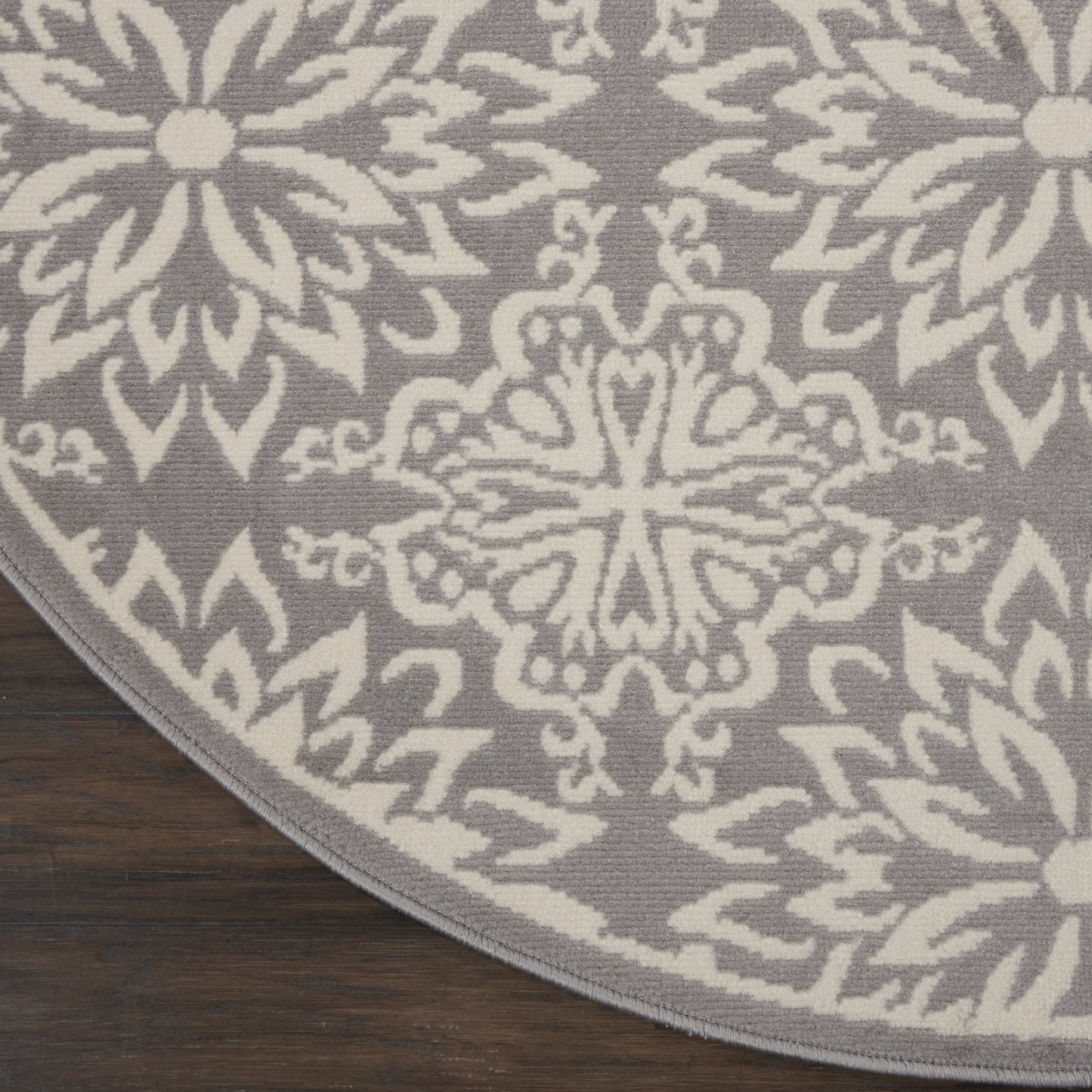 Round gray rug with white geometric floral mandala pattern on dark wood floor.