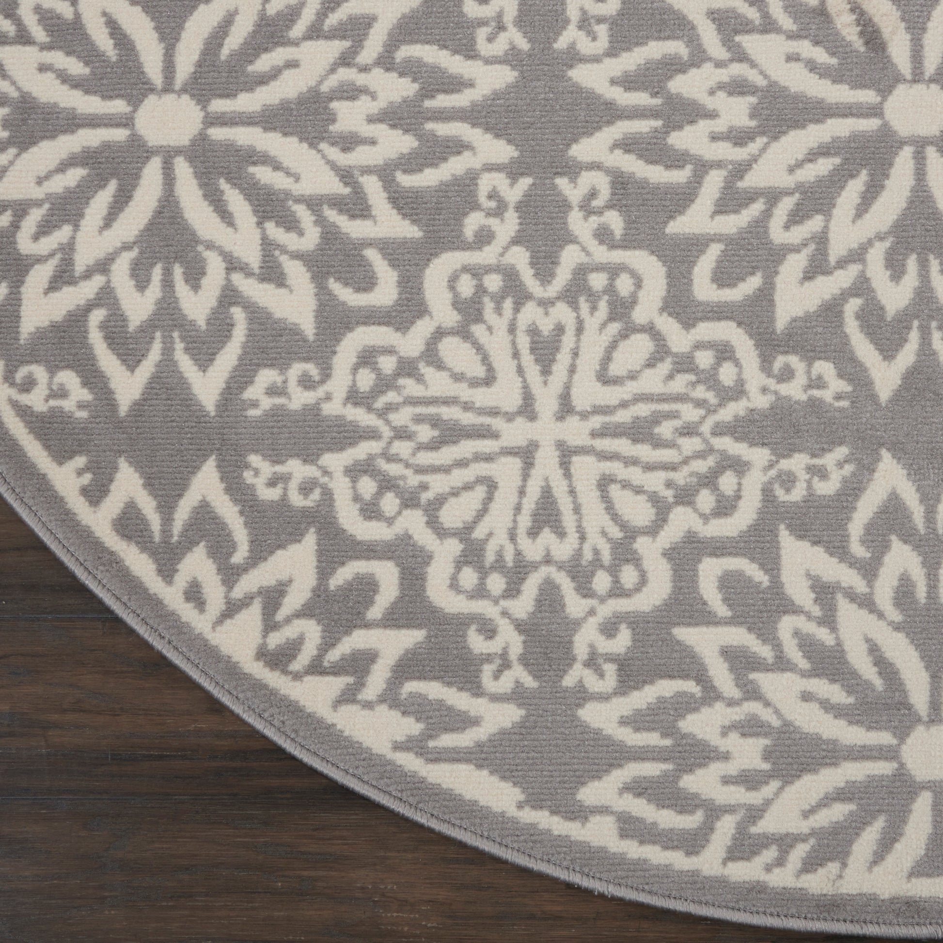 Round gray rug with white geometric floral mandala pattern on dark wood floor.