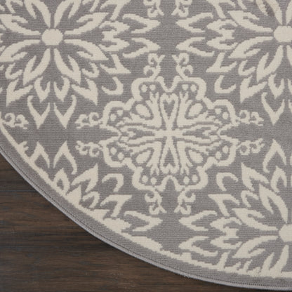 Round gray rug with white geometric floral mandala pattern on dark wood floor.