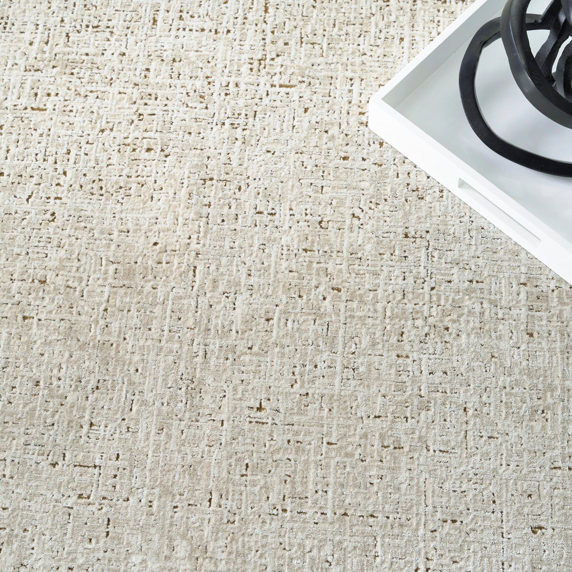 Beige textured rug with a white rectangular tray and black circular metal rings.