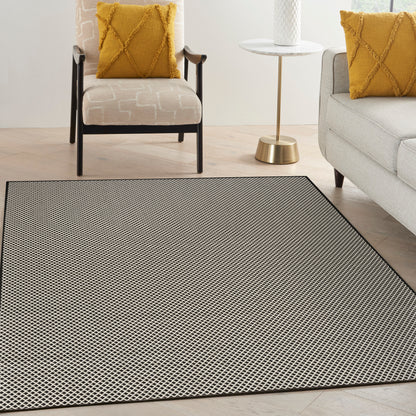 Living room with a large dotted area rug, beige patterned armchair with a mustard pillow, light gray sofa, and a white-and-gold side table.