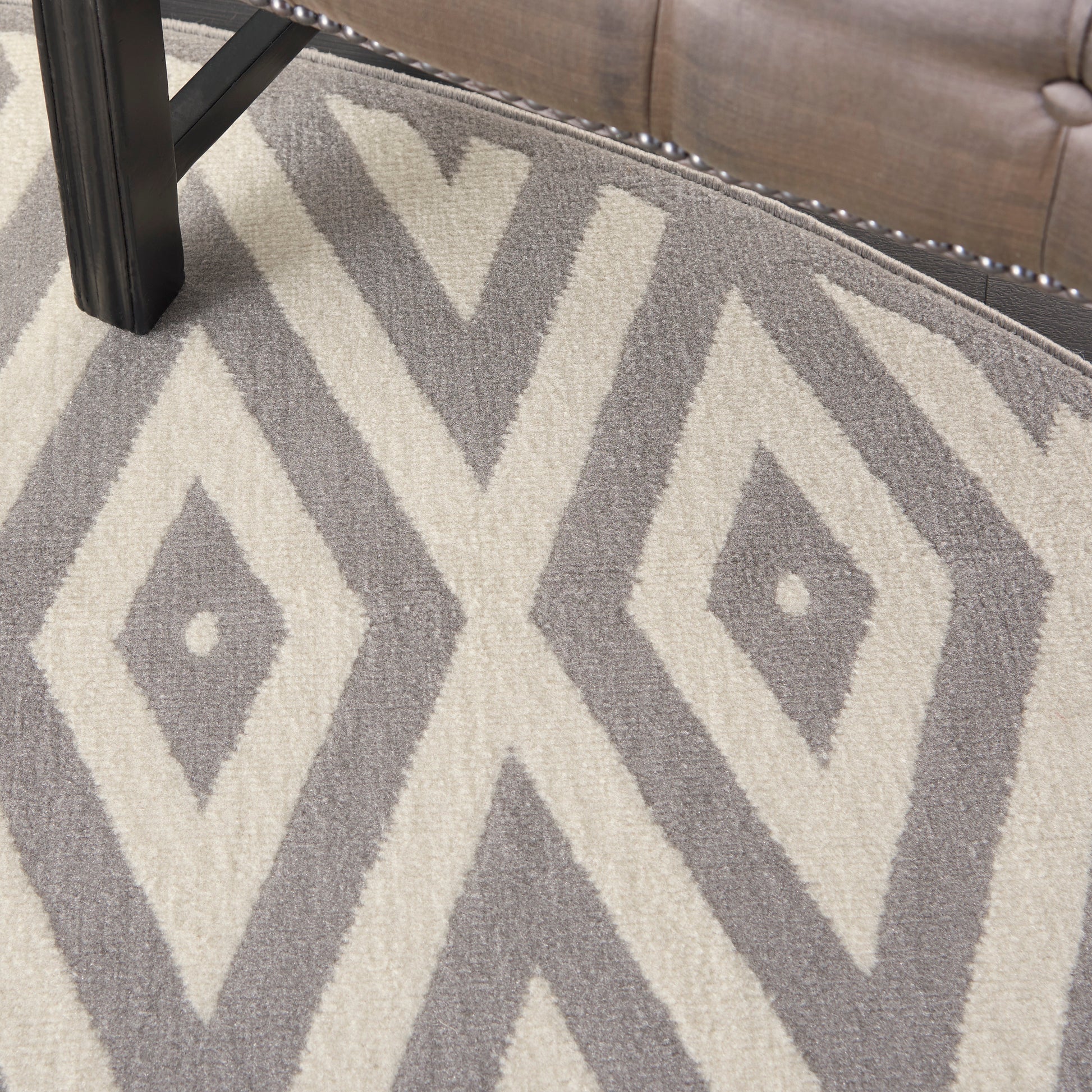 Gray and ivory geometric diamond rug, 8' round, with bold diamond motifs; placed next to a tufted sofa with nailhead trim.