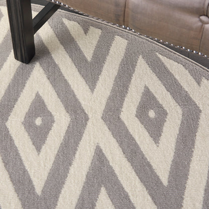 Gray and ivory geometric diamond rug, 8' round, with bold diamond motifs; placed next to a tufted sofa with nailhead trim.