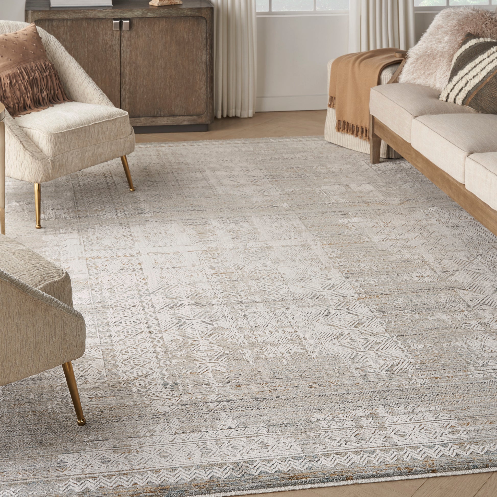 Neutral living room with a textured geometric area rug, cream upholstery, and mid-century chairs with gold legs.