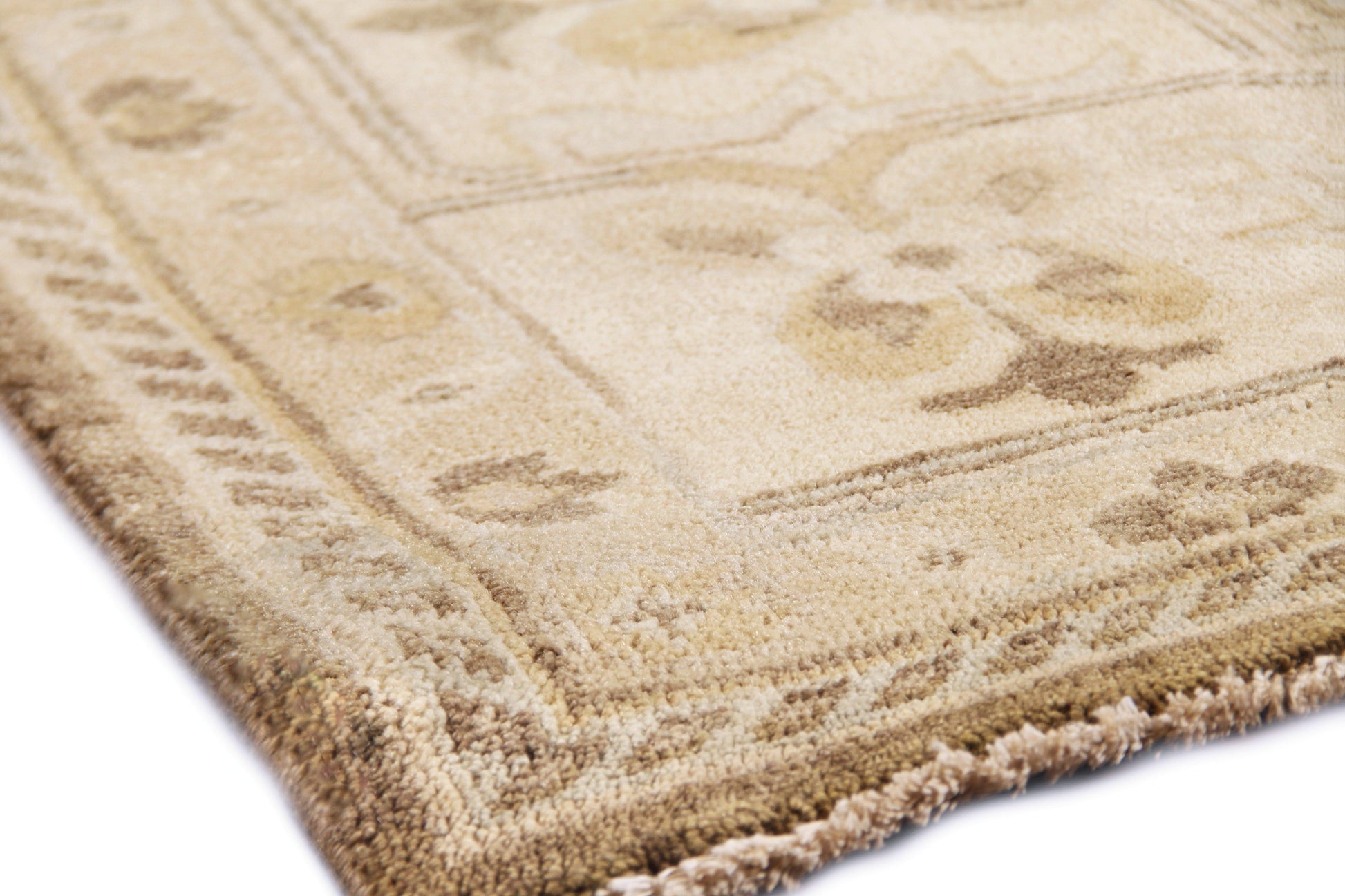 Beige oriental-style rug corner with floral border, cream and tan hues and fringed edge.