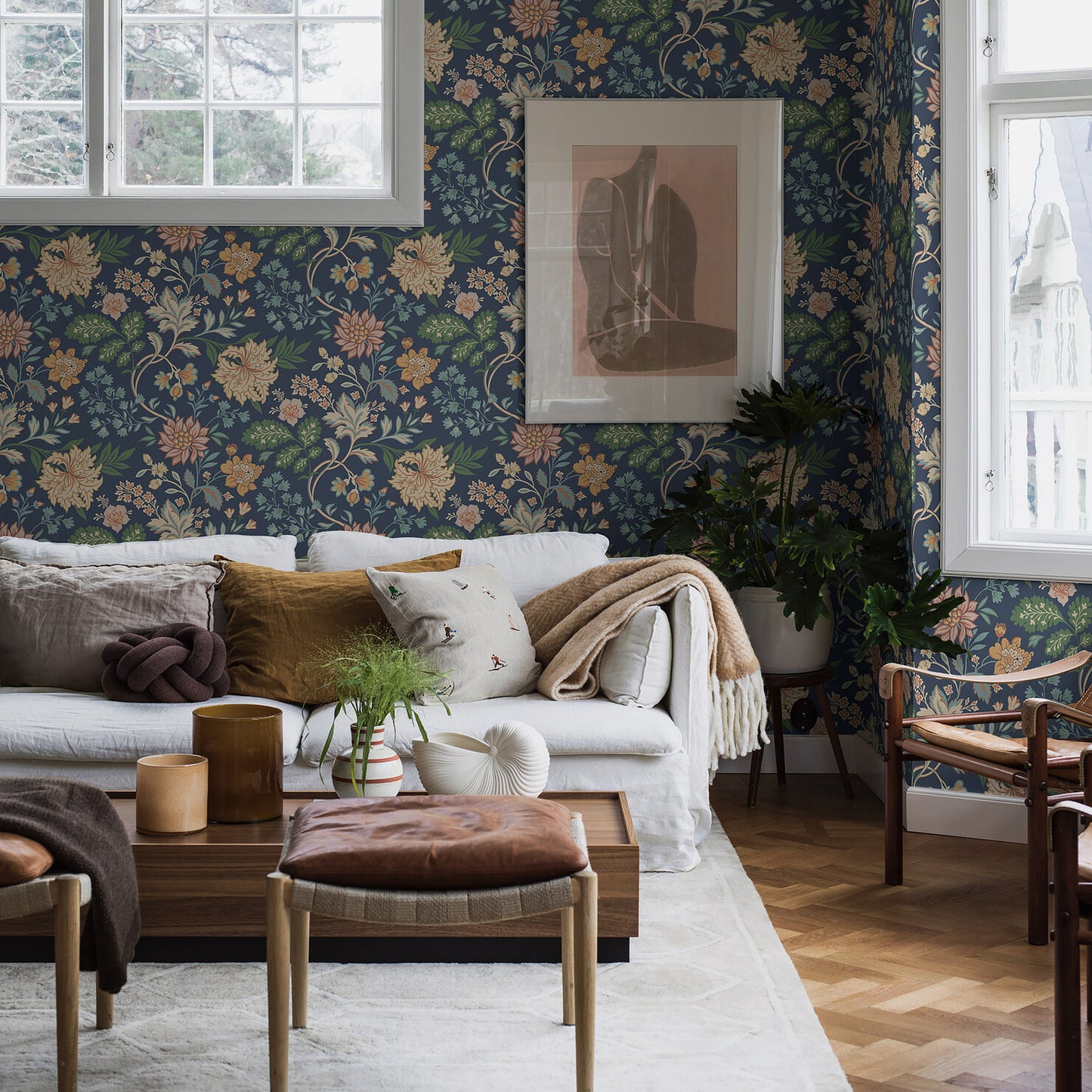 Cozy living room with navy floral wallpaper, gray sofa, mustard cushions, wooden coffee table, plants, and framed art.