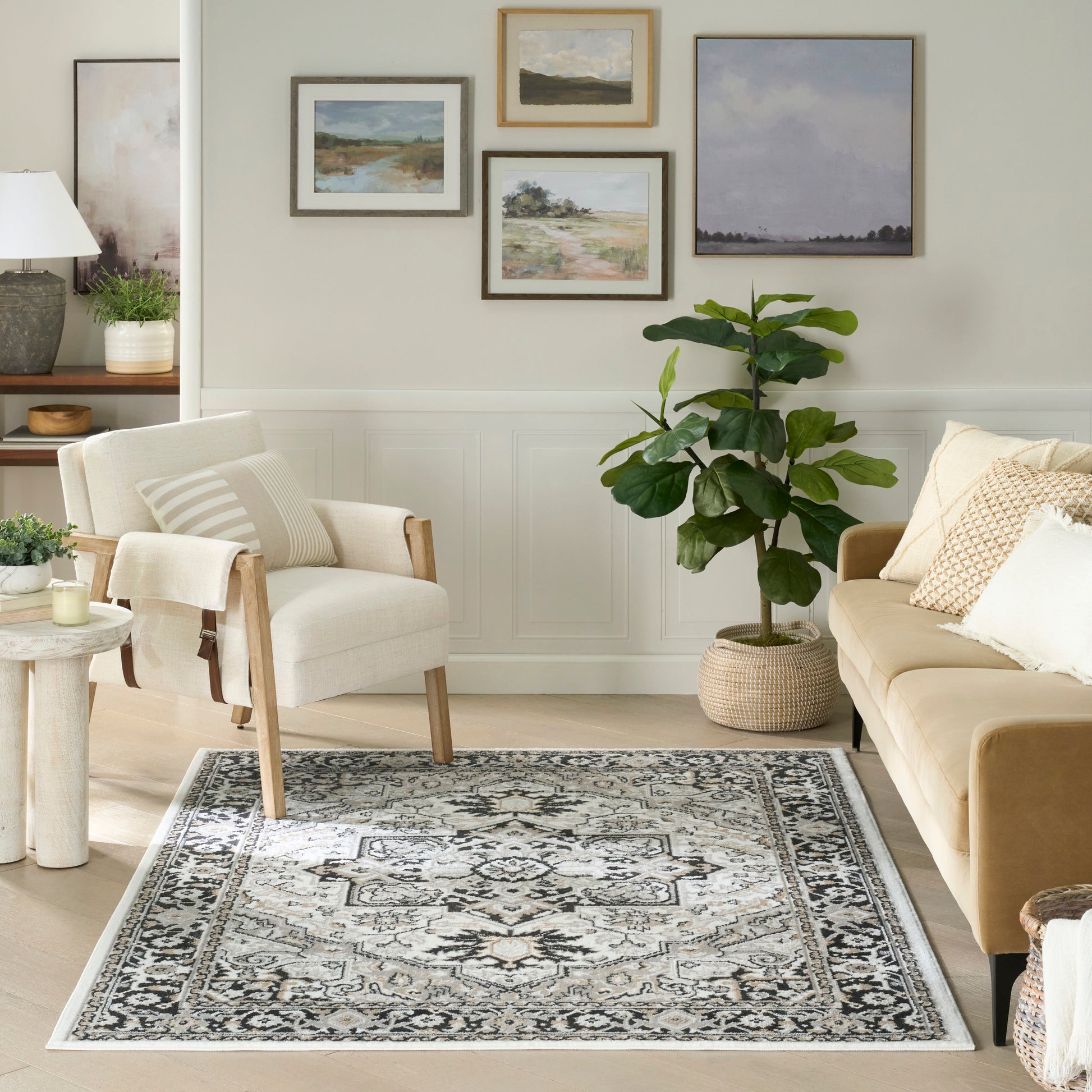 Rectangular area rug with gray, ivory and black oriental pattern in a light living room with beige sofa, armchair and plants.