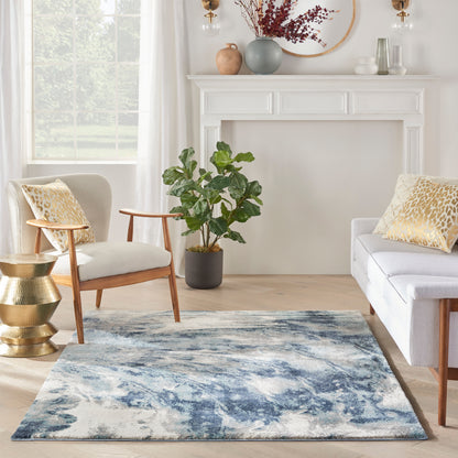 Bright living room with blue abstract rug, mid-century chair, white sofa with gold pillows, potted plant, and white mantel.