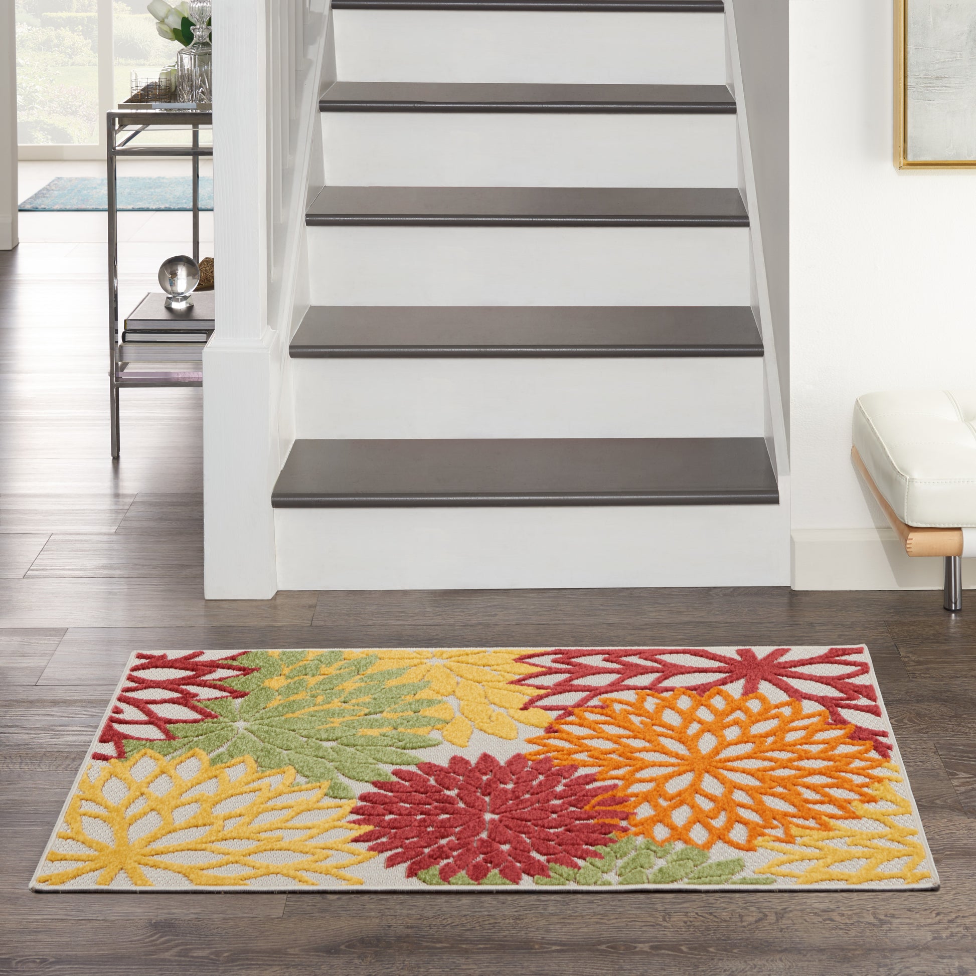 Colorful floral area rug with yellow, red and orange blossoms on dark wood floor by a white staircase.