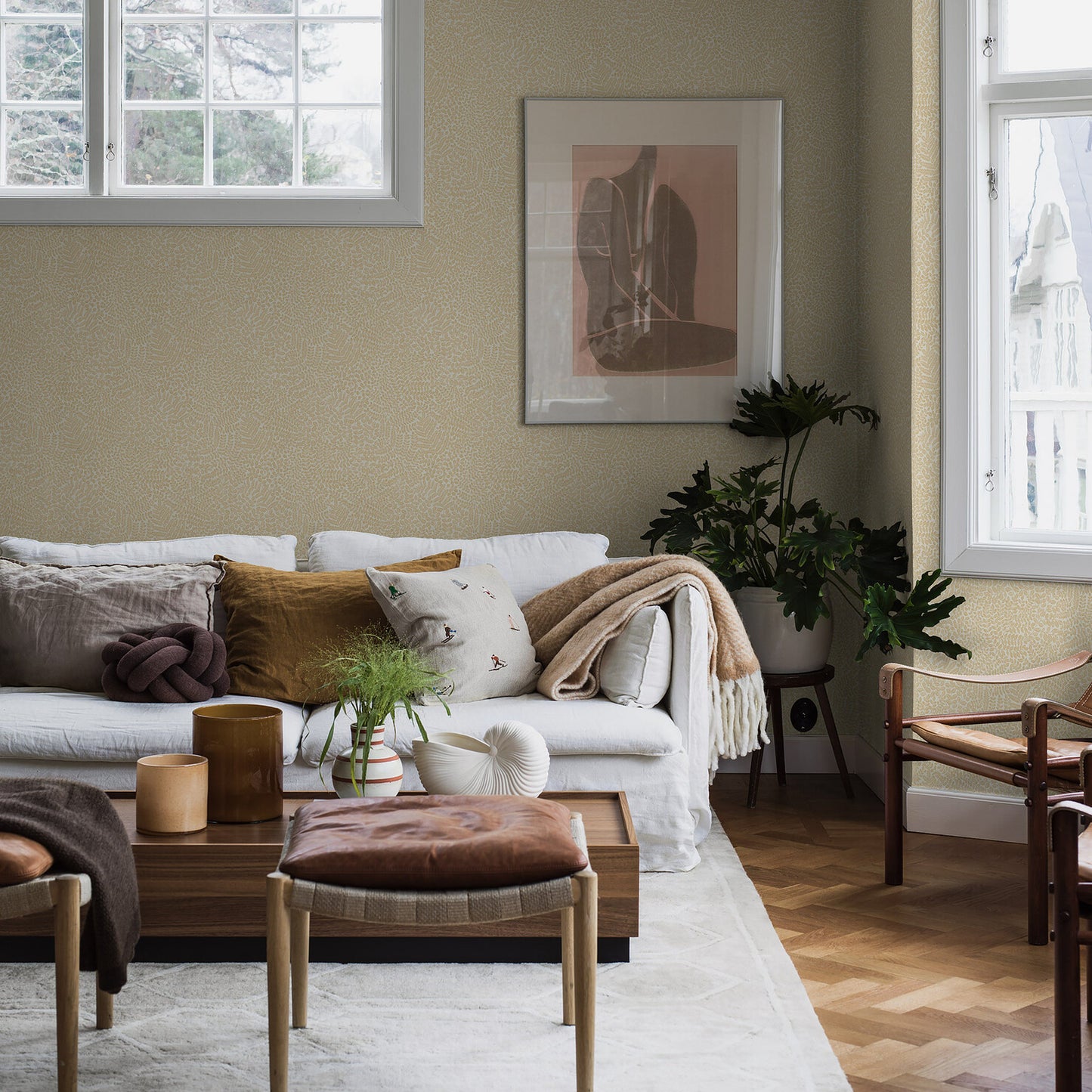 Beige living room with subtle patterned wallpaper on the wall behind a sofa, coffee table and plants.