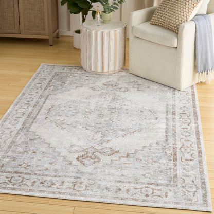 Soft gray distressed area rug with beige border in a cozy living room beside a cream armchair and round wood side table.
