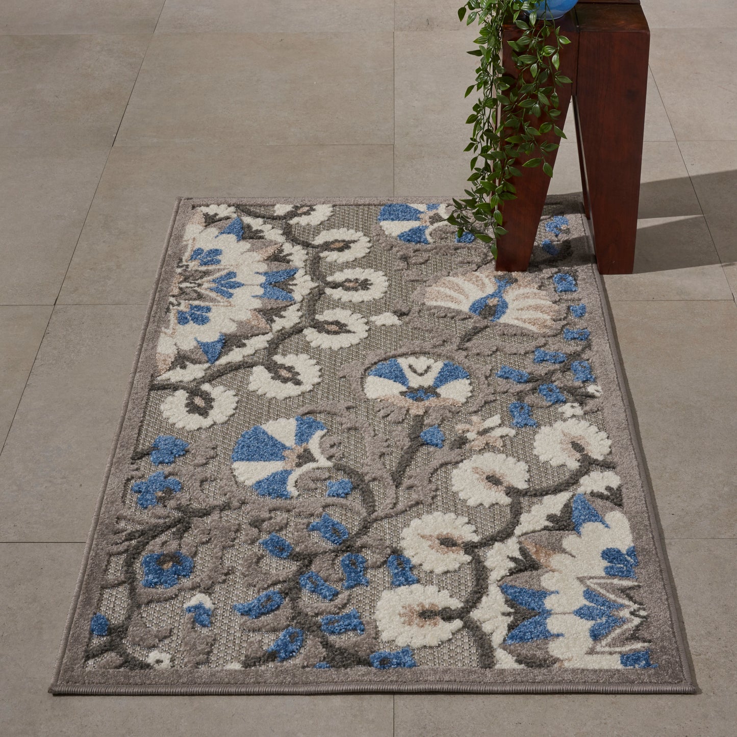 Rectangular area rug with gray base and white/blue floral pattern; tufted, low-pile synthetic fibers, for living room or entryway.