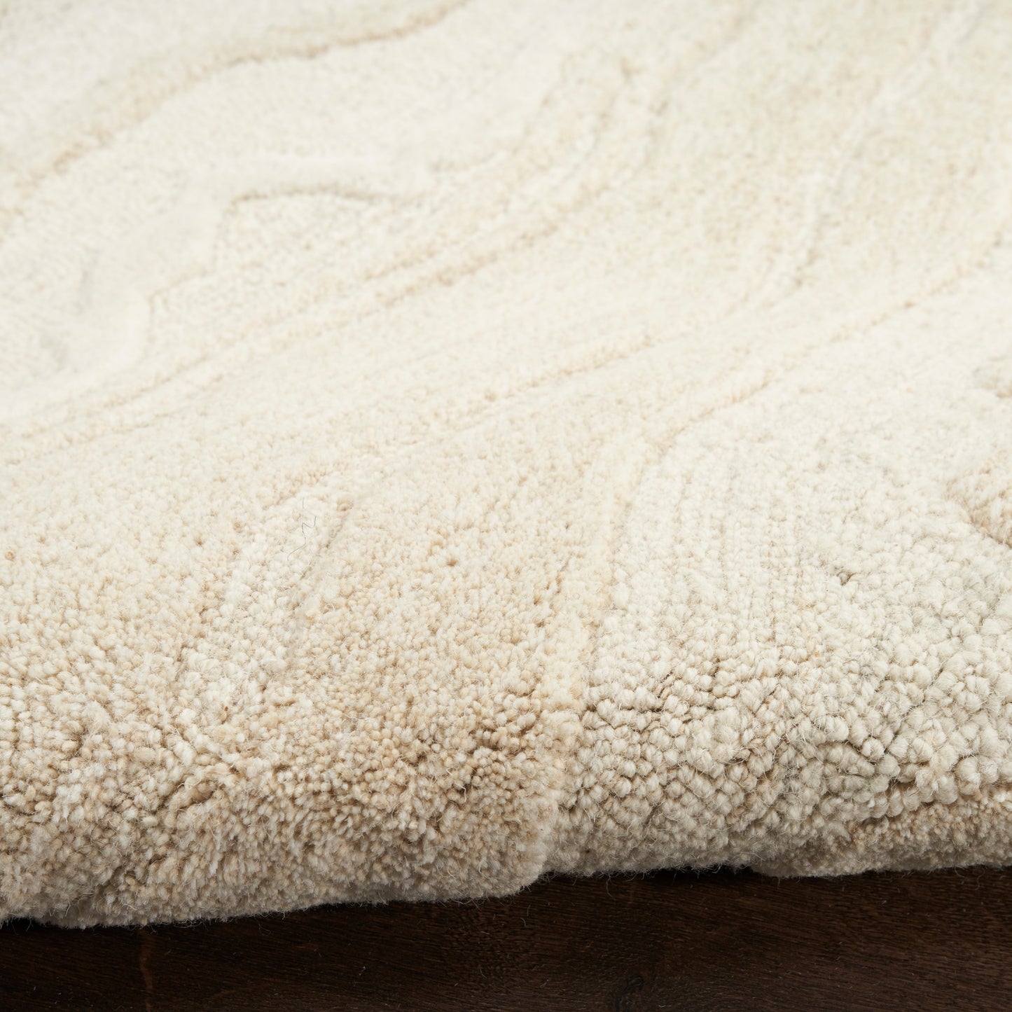 Cream shag rug with dense loop pile and rolled edge on dark wood floor.
