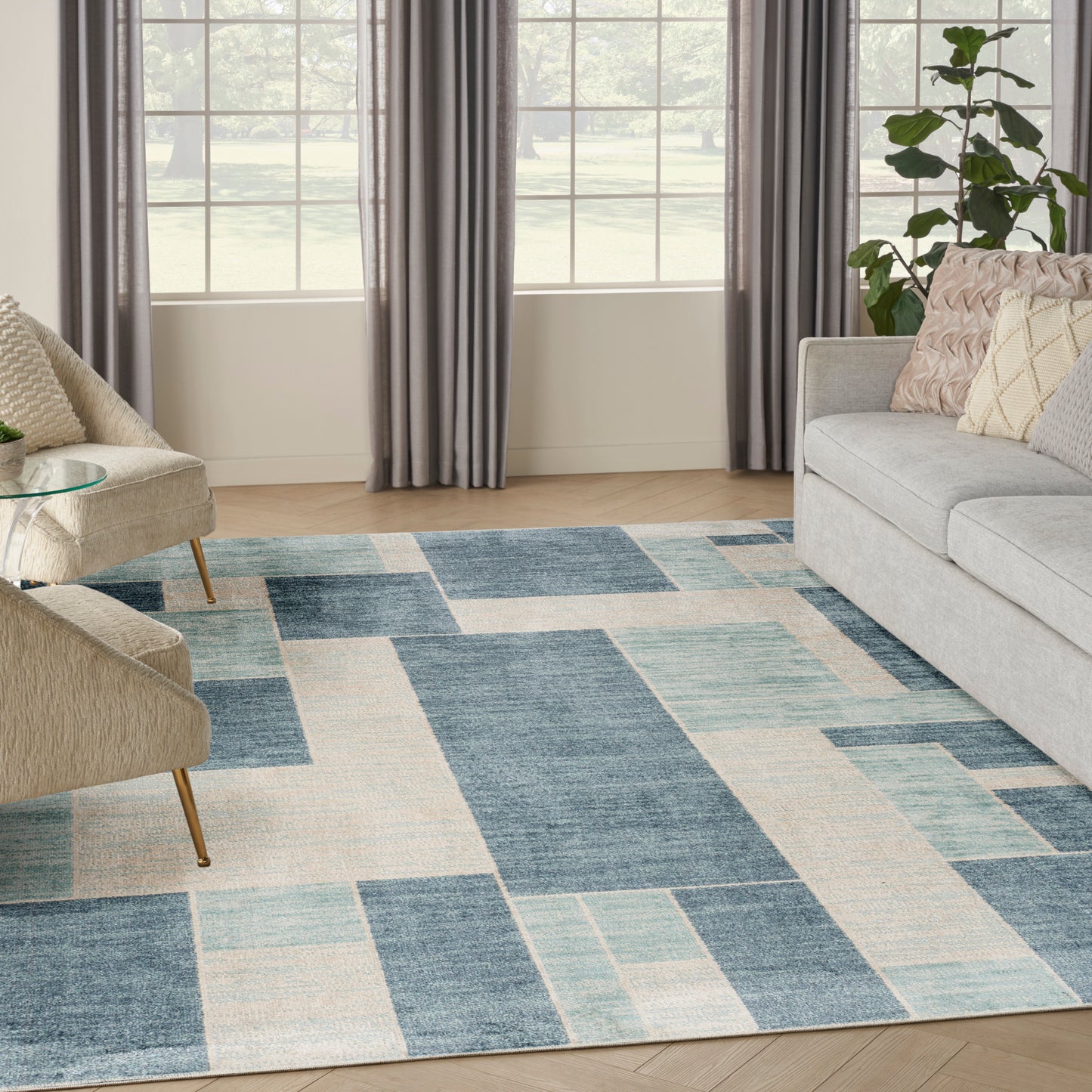 Blue and ivory geometric area rug in a modern living room with gray sofa, beige chairs, and large windows.