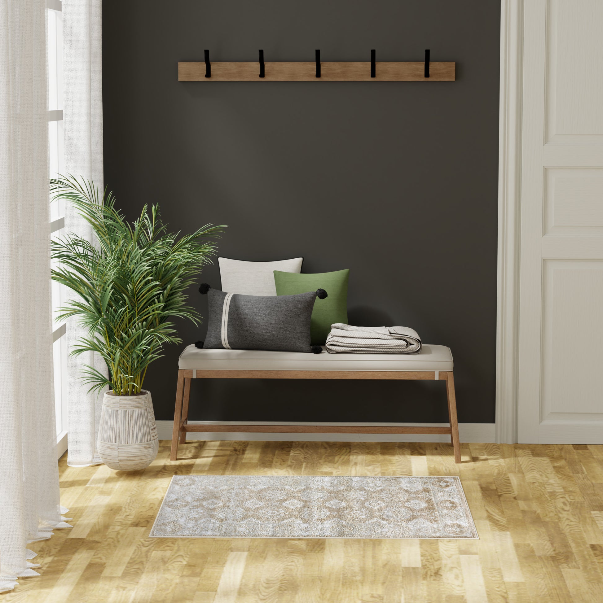 Wooden hall bench with cream cushion and green/gray pillows on a dark wall, with a five-hook coat rack, plant, and beige rug.