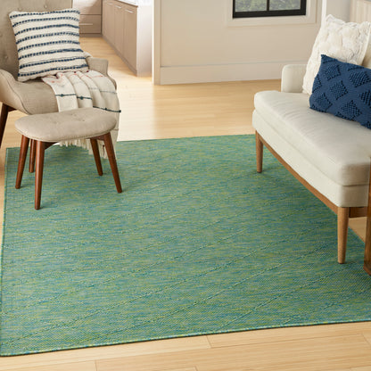 Teal woven area rug with subtle texture on a light wood floor, paired with beige mid-century chairs, an ottoman, and blue cushions.