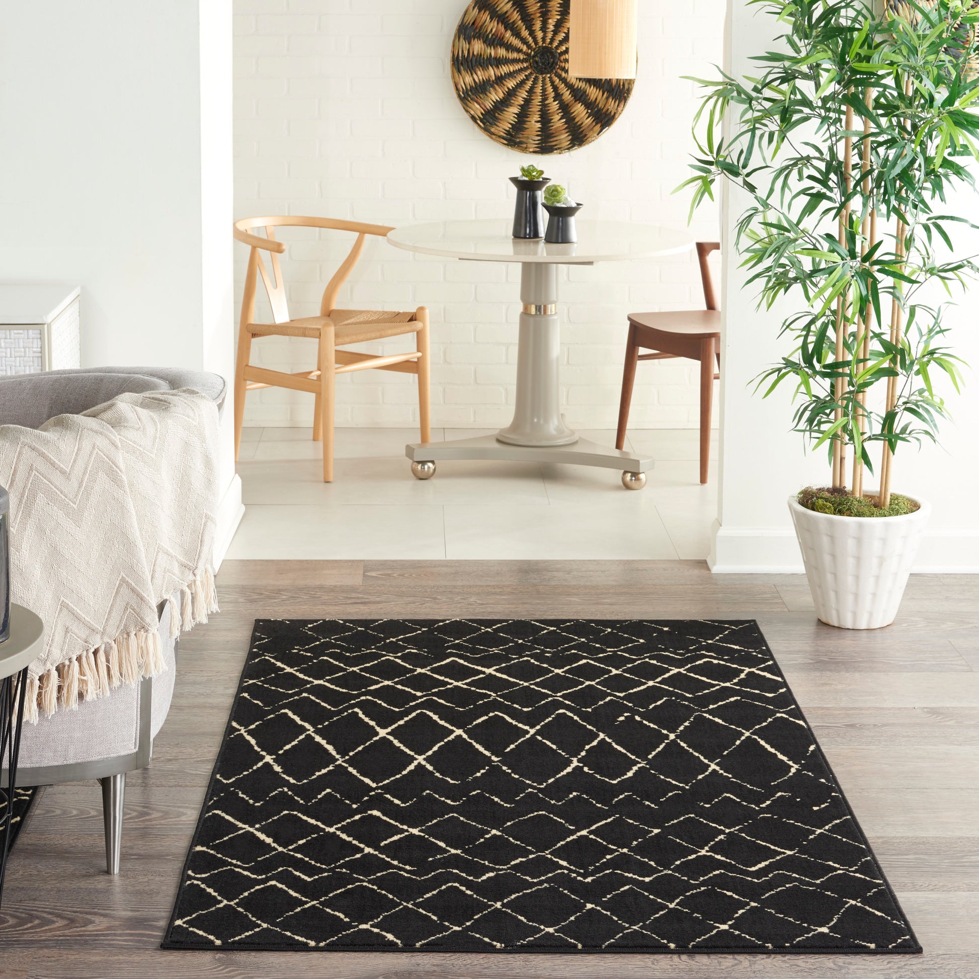 Black rug with white lattice pattern on light wood floor in a bright living room with a round glass table.