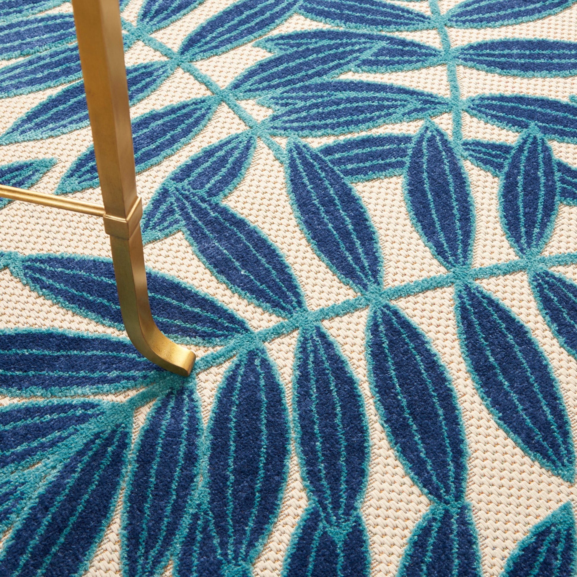 Round tropical rug with a white textured background and teal blue leaf pattern.