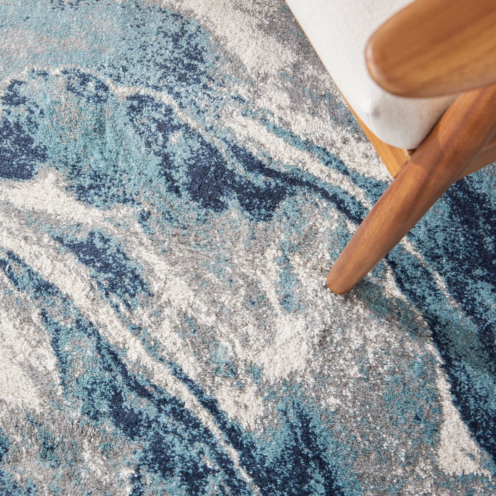 Abstract blue area rug with white streak patterns; wooden chair leg resting on its edge.