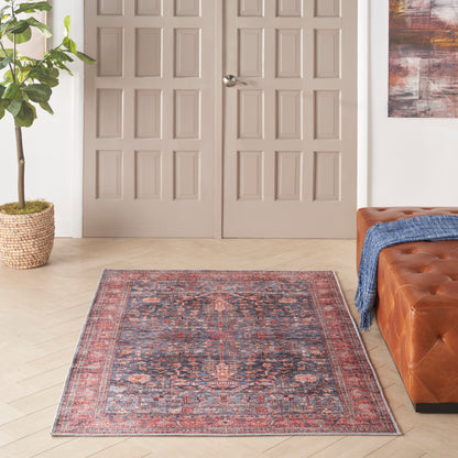 Oriental rug with red-blue pattern on light wood floor, beige paneled doors, potted plant, tufted brown leather sofa.