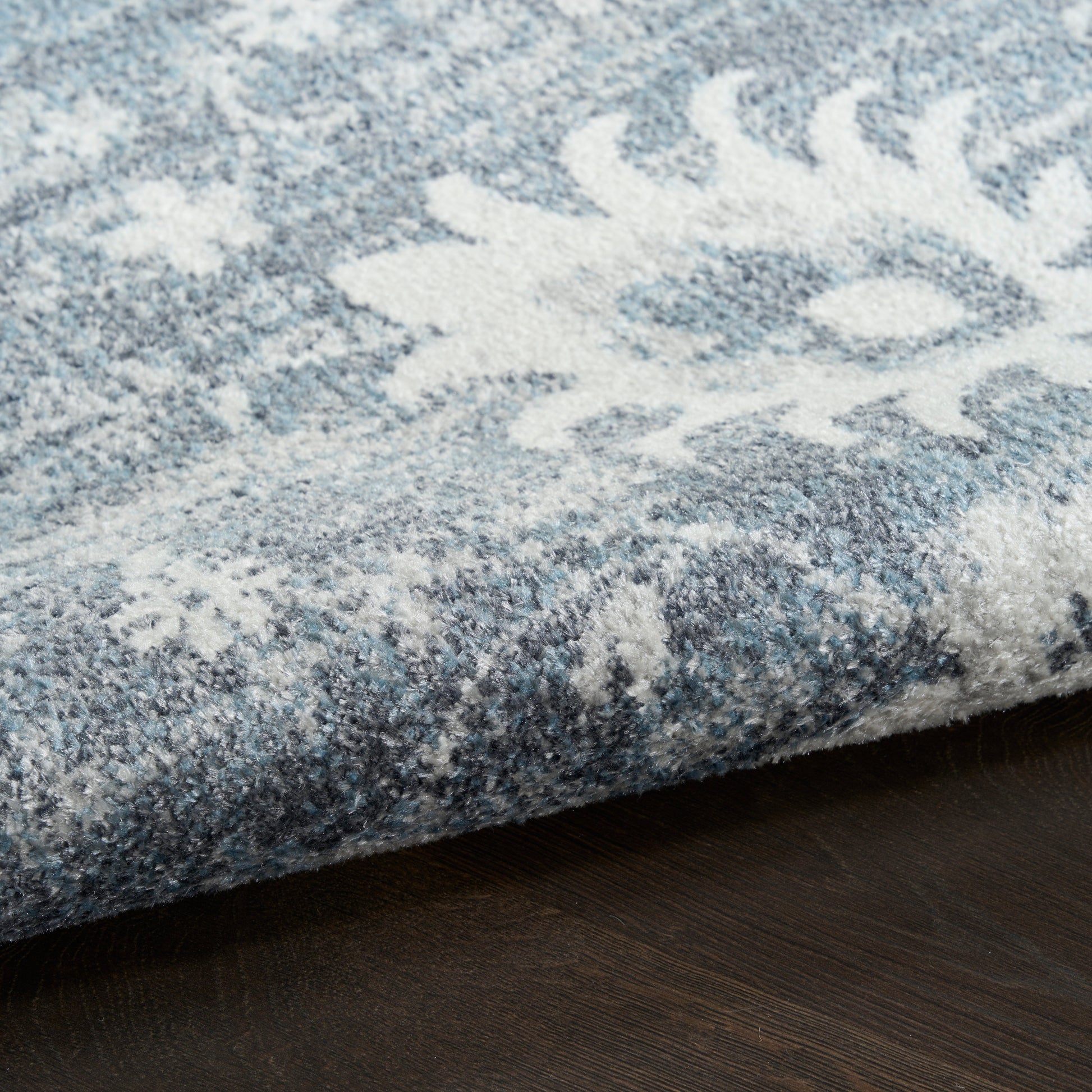 Blue and white snowflake-pattern rug with plush pile, folded edge on dark wood floor.