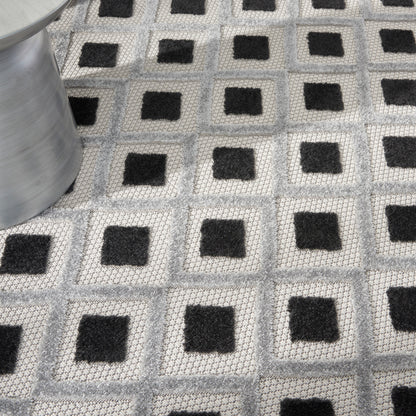 Geometric gray woven rug with repeating light-gray squares and black centers; modern floor mat, metal roll visible on left.