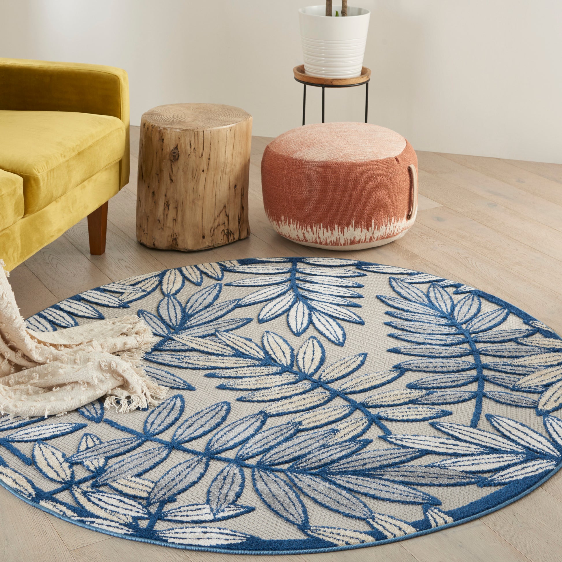 Round blue and white leaf-pattern rug on light wood floor; mustard sofa and wooden stools visible in cozy living space.