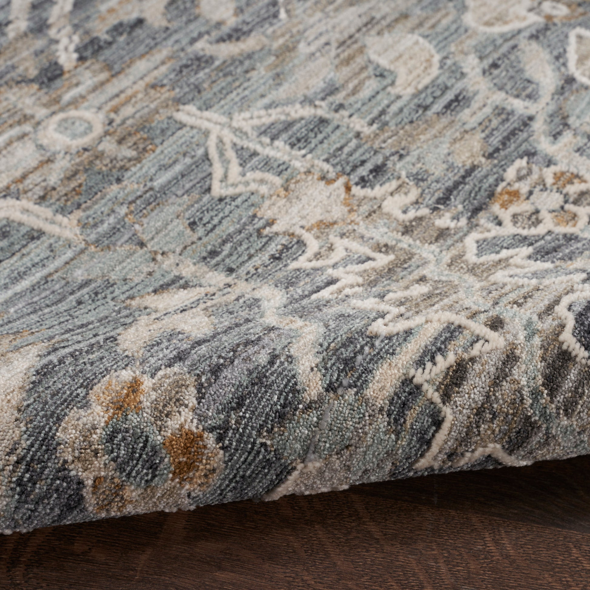 Blue-gray rug with ivory floral motifs, textured plush pile and folded edge.