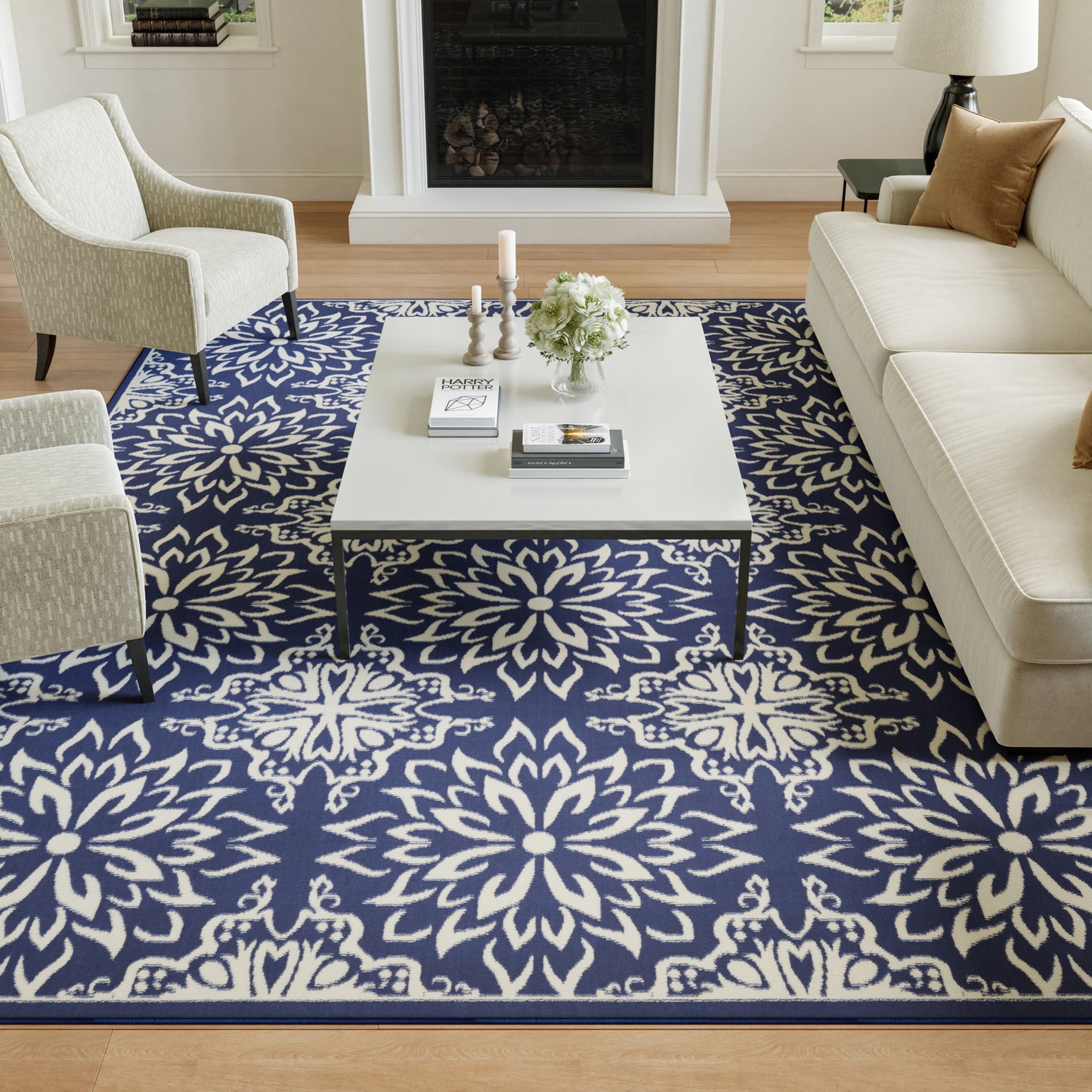 Living room scene with navy blue and white floral rug, cream sofa, light armchairs, and a white coffee table.