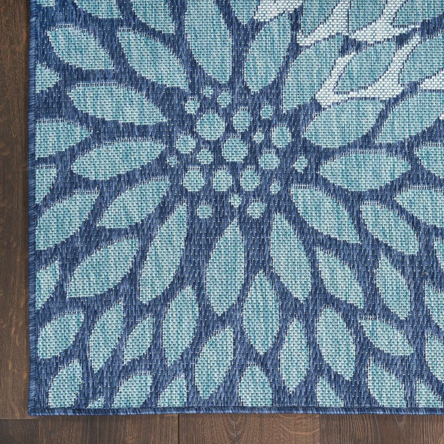 Teal and navy blue woven rug with a large floral motif radiating from a central cluster on dark wood floor.