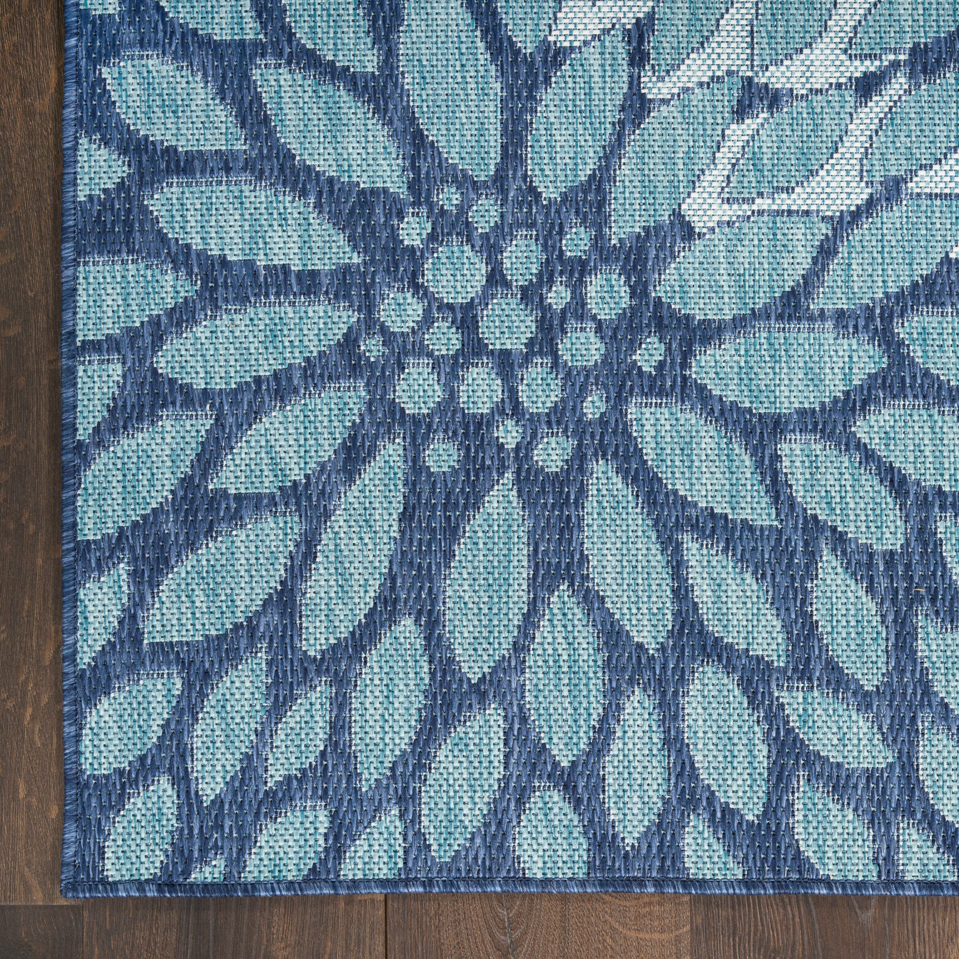 Teal and navy blue woven rug with a large floral motif radiating from a central cluster on dark wood floor.