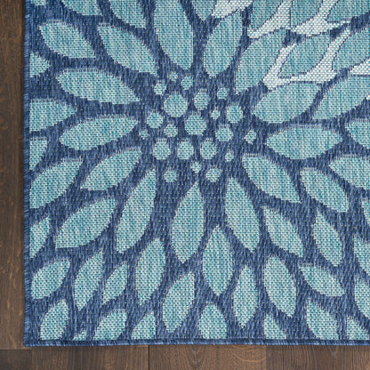 Teal and navy blue woven rug with a large floral motif radiating from a central cluster on dark wood floor.